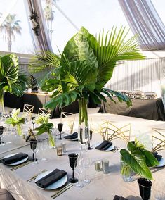 the table is set with black and white plates, silverware, and palm trees