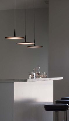 three lights hanging from the ceiling above a bar with stools and wine glasses on it