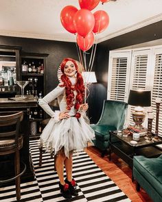 a woman with red hair wearing a white tutu and holding balloons in her hand