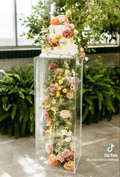 a three tiered wedding cake with flowers on the top is surrounded by greenery