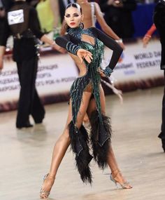 a woman in a green and black dress is dancing with feathers on her leg while people watch