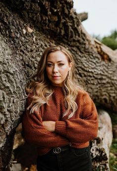 a woman leaning against a tree with her arms crossed