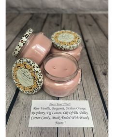 three jars of pink candles sitting on top of a wooden table next to a note