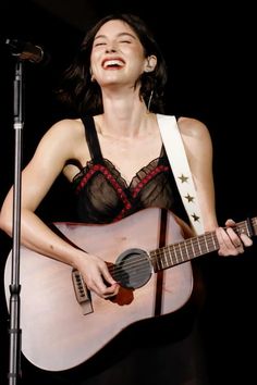 a woman holding a guitar and singing into a microphone