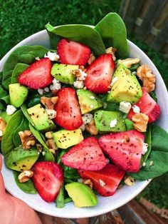 a white bowl filled with spinach, strawberries and avocado on top