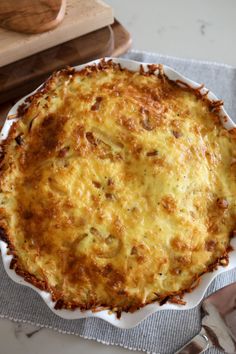 a cheesy casserole on a white plate next to a cutting board