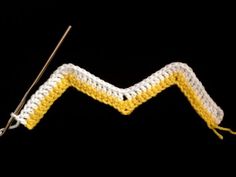 a yellow and white crochet chevron stitch on a black background with a knitting needle