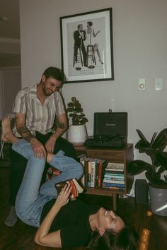 a man and woman sitting on the floor in front of a table with some books