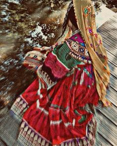 a woman in a colorful dress walking on a wooden walkway next to trees and water