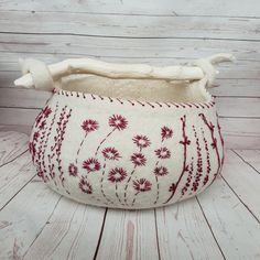 a white and red basket with flowers on the inside is sitting on a wooden floor