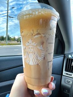 a woman holding up a cup of coffee in her car