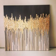 an abstract painting with gold and black trees on the bottom, against a white wall