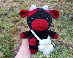 a hand holding a crocheted black and white cow with a flower in it's mouth