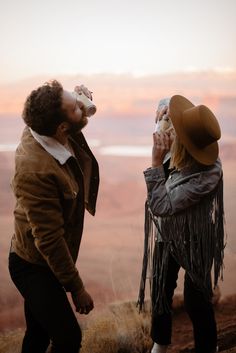 a man and woman standing next to each other on top of a hill drinking from bottles