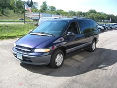 a blue van parked in a parking lot next to other cars on the side of the road