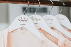 three white hangers with names on them are hanging from a wooden rail in front of a pink dress