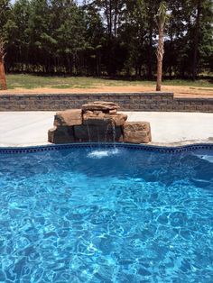 an empty swimming pool with blue water and rocks on the edge, surrounded by trees