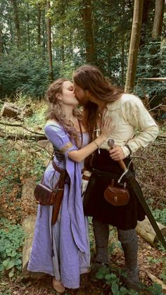 a man and woman are kissing in the woods with swords on their heads, wearing medieval clothing