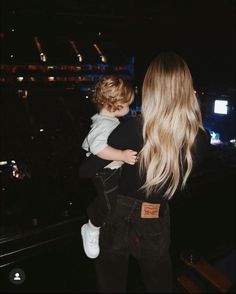 a woman holding a small child in her arms at a concert with the lights on