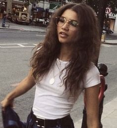 a woman with long hair and glasses is standing on the sidewalk