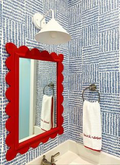 a bathroom with blue and white wallpaper, red framed mirror, sink and faucet