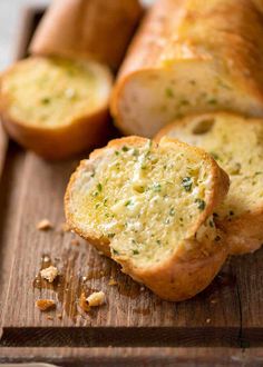 two pieces of bread sitting on top of a wooden cutting board next to garlic and parmesan cheese