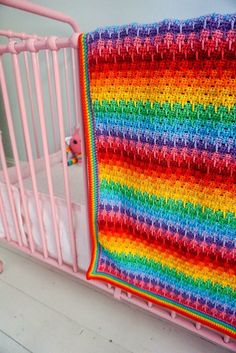 a crocheted blanket hanging on the side of a pink crib