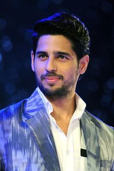 a man wearing a suit and tie standing in front of a dark background with lights