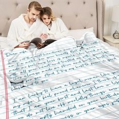 a man and woman sitting on top of a bed under a blanket with writing on it