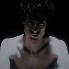 a man with black hair and no shirt in the dark