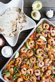 a pan filled with shrimp and vegetables next to tortillas