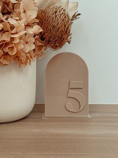 a white vase filled with flowers next to a wooden table number five sign on top of a wood floor