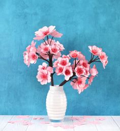 a white vase filled with pink flowers on top of a table