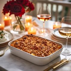 a casserole dish on a table with candles and wine glasses