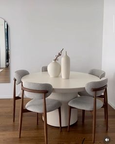 a white table with four chairs around it and two vases on the top one