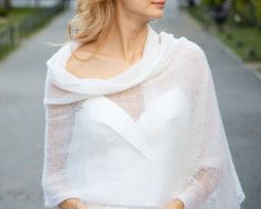 a woman wearing a white shawl standing on the side of a road with her hands in her pockets