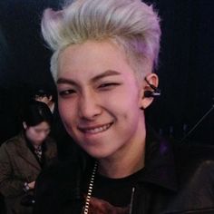 a young man with blonde hair and piercings smiles at the camera while wearing a black jacket