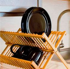 a wooden rack holding black plates and pans on a counter top next to a sink