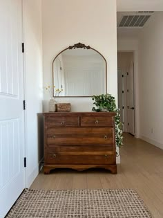 a wooden dresser sitting in front of a mirror on top of a white wall next to a doorway