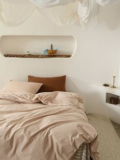 an unmade bed in a bedroom with white walls and drapes hanging from the ceiling