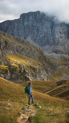 a man with a backpack is standing on a path in front of a mountain range