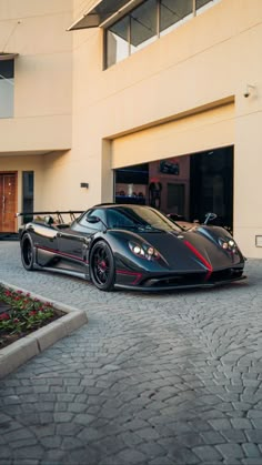 a black and red sports car parked in front of a large building on a cobblestone driveway