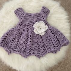 a purple crocheted dress with a white flower on the front and side, sitting on a furry rug