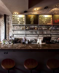 a bar with three stools in front of it and menus on the wall