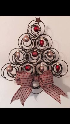 a metal christmas tree with red balls and bows on it's head, hanging from a wall