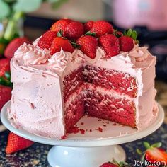 a strawberry cake with one slice cut out and strawberries on the plate next to it