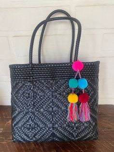 a black woven tote bag with colorful pom - poms