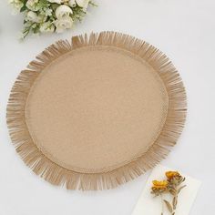 a round place mat with fringes on it next to some flowers and a napkin