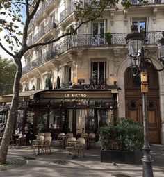 an old building with tables and chairs on the street in front of it, next to a lamp post