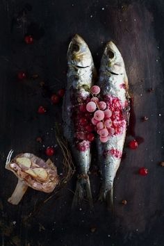 two fish on a table with some red berries and other food items around the fish